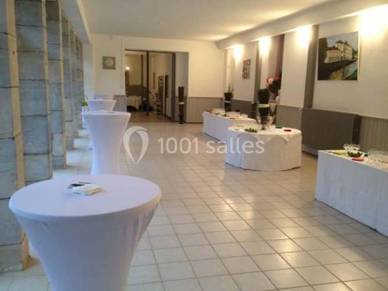 Salle lumineuse avec tables hautes et buffets dressés, prête pour un événement ou une réception.