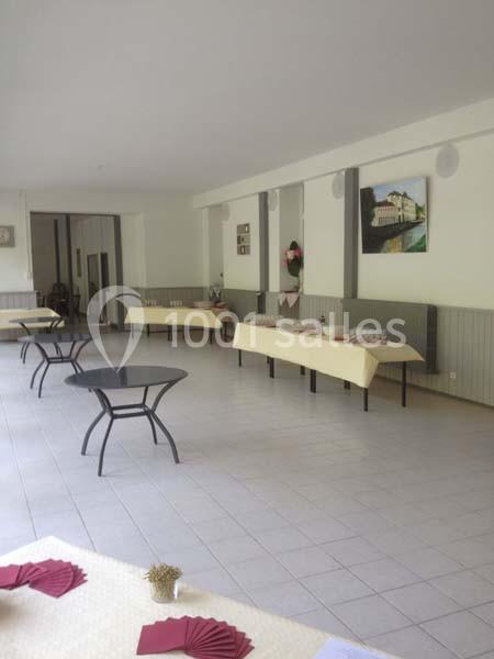 Salle lumineuse avec tables recouvertes de nappes claires, chaises noires et décorations discrètes sur les murs.