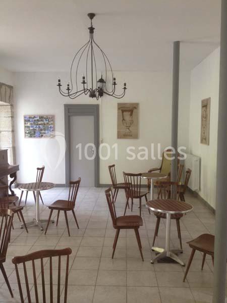 Salle lumineuse avec des chaises en bois, des tables rondes, un lustre suspendu et des décorations murales.