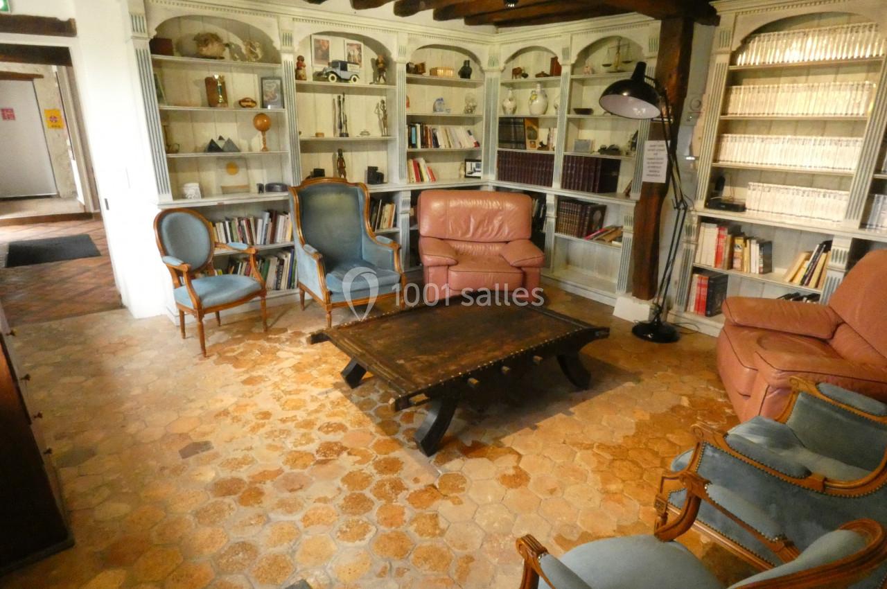 Salle de lecture avec fauteuils, table basse en bois, étagères remplies de livres et éclairage chaleureux.