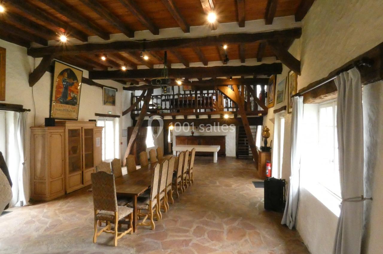Salle spacieuse avec une grande table en bois entourée de chaises, poutres apparentes et lumière naturelle.