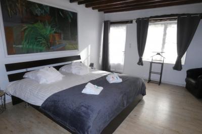 Salle de bain lumineuse avec baignoire encastrée sur estrade carrelée, poutres apparentes et grande fenêtre.