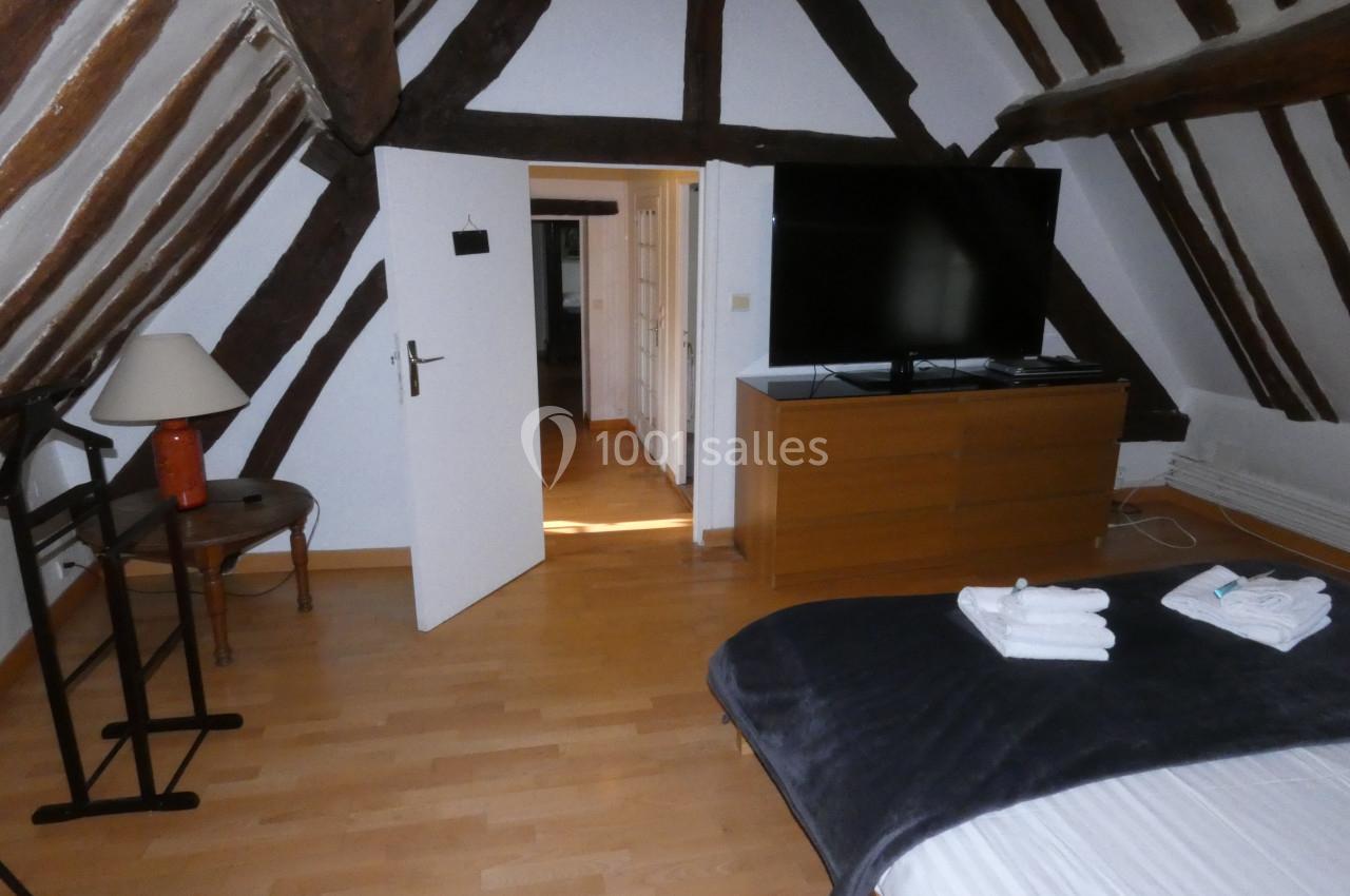 Chambre mansardée avec poutres apparentes, lit double, télévision sur meuble en bois et sol en parquet clair.