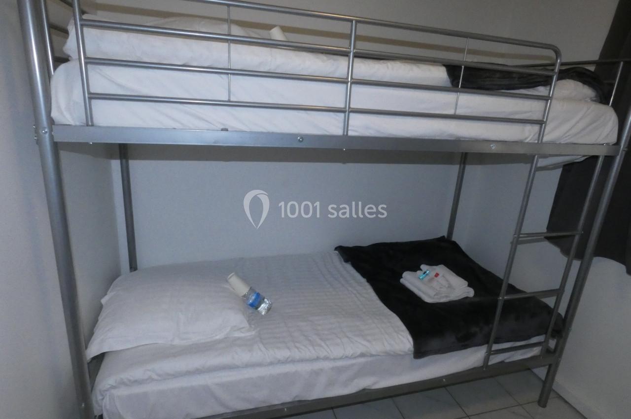 Lit superposé en métal avec matelas blancs, couvertures sombres et serviettes pliées sur le lit du bas.