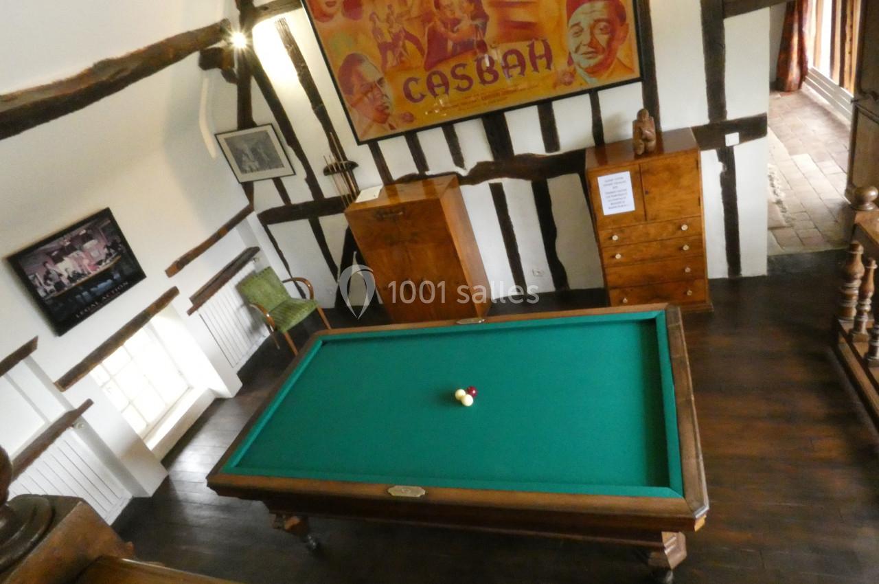 Table de billard avec deux boules, située dans une pièce rustique avec poutres apparentes et affiches murales.
