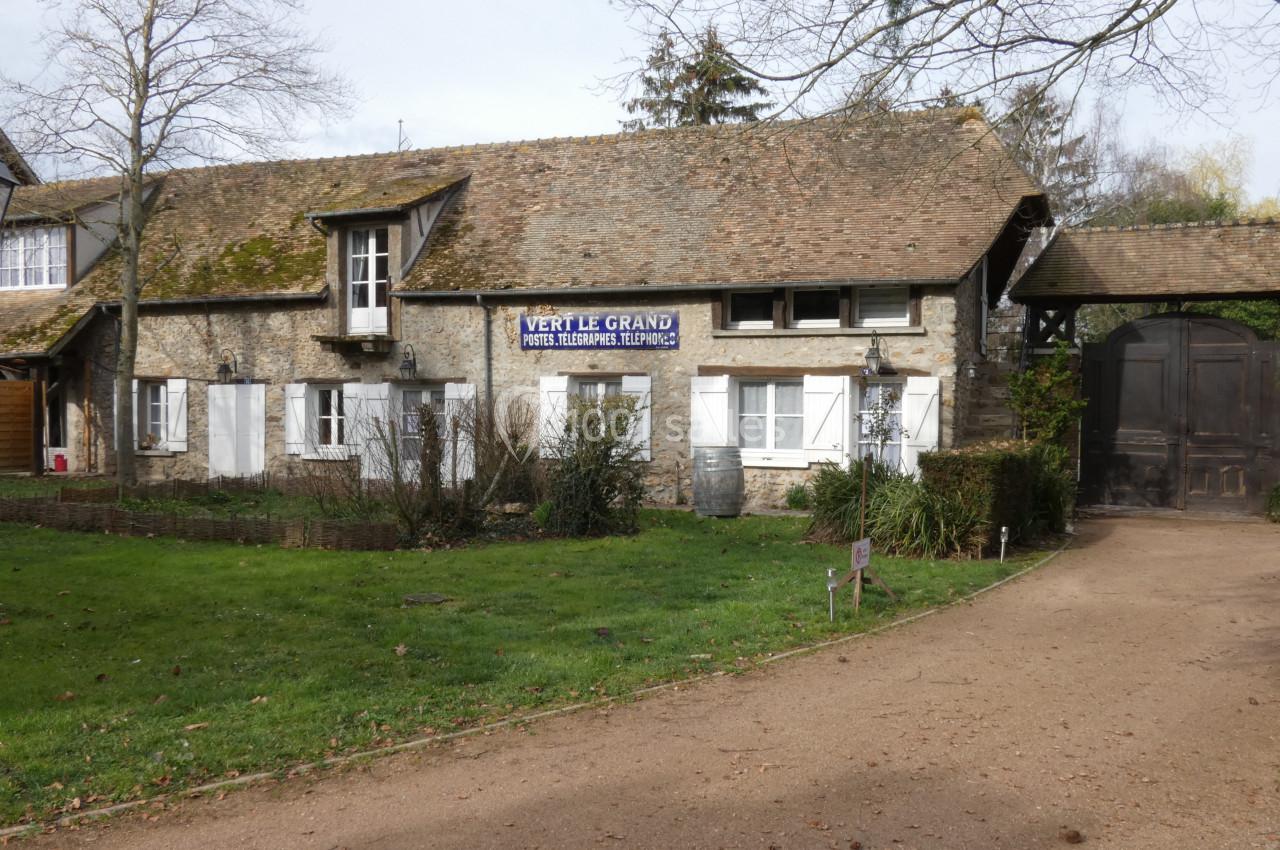 Façade d'une maison en pierre avec volets blancs, toit en tuiles et une allée bordée de pelouse.