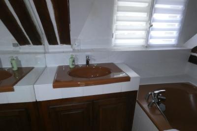 Salle de bain lumineuse avec baignoire encastrée sur estrade carrelée, poutres apparentes et grande fenêtre.