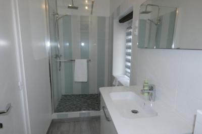 Salle de bain lumineuse avec baignoire encastrée sur estrade carrelée, poutres apparentes et grande fenêtre.