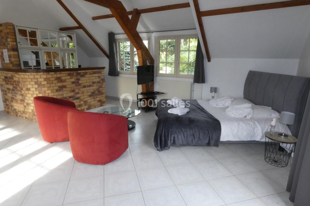 Chambre lumineuse avec lit double, fauteuils rouges, table basse, télévision et grande fenêtre donnant sur un jardin.