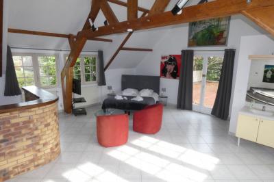 Salle de bain lumineuse avec baignoire encastrée sur estrade carrelée, poutres apparentes et grande fenêtre.