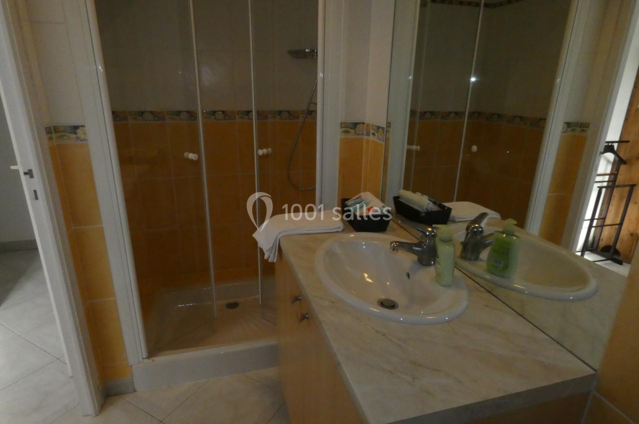 Salle de bain avec une douche à parois vitrées, un lavabo double et des articles de toilette sur le plan de travail.