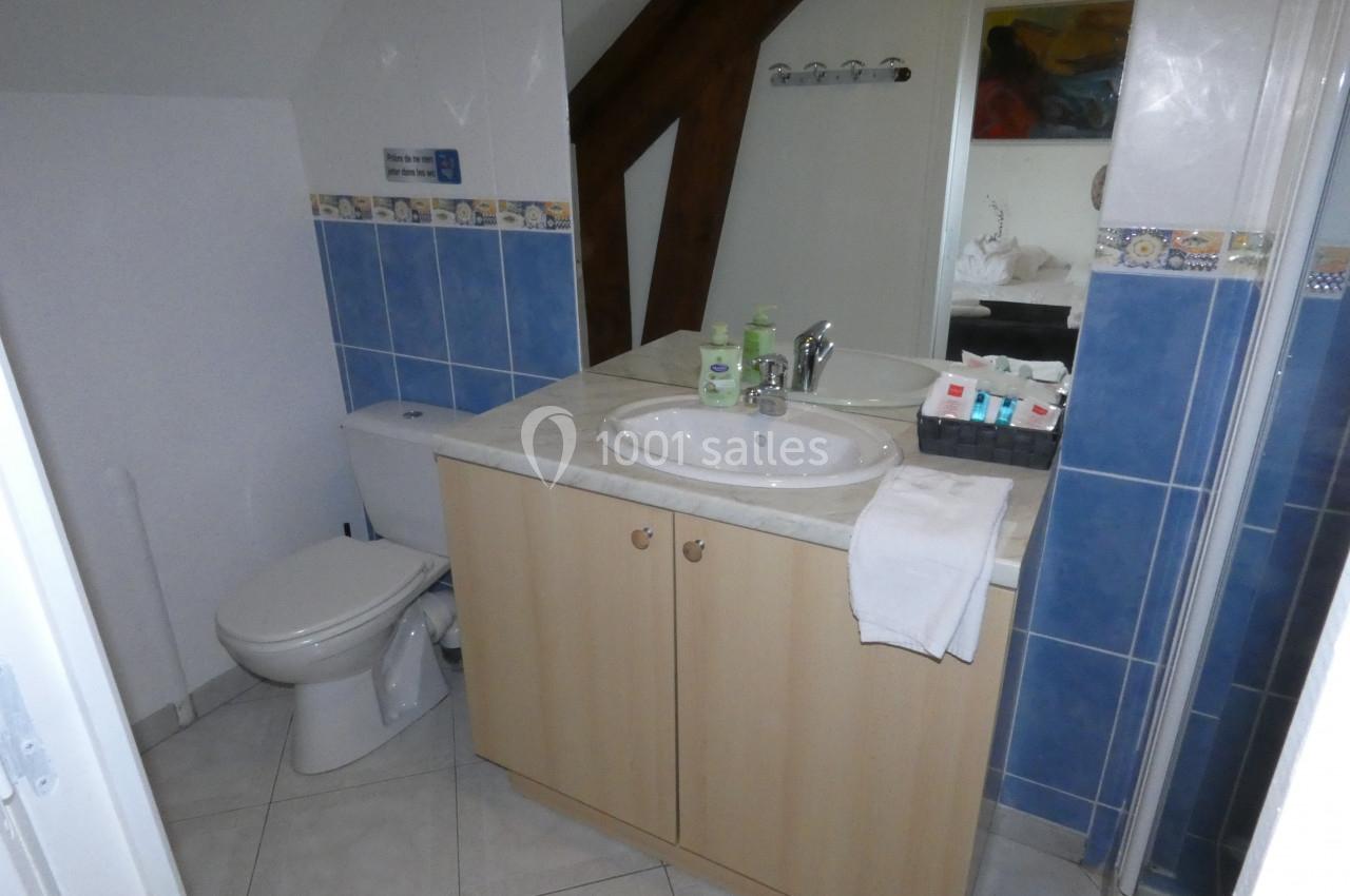 Salle de bain avec lavabo, miroir, toilettes, douche, produits de toilette et carrelage bleu sur les murs.