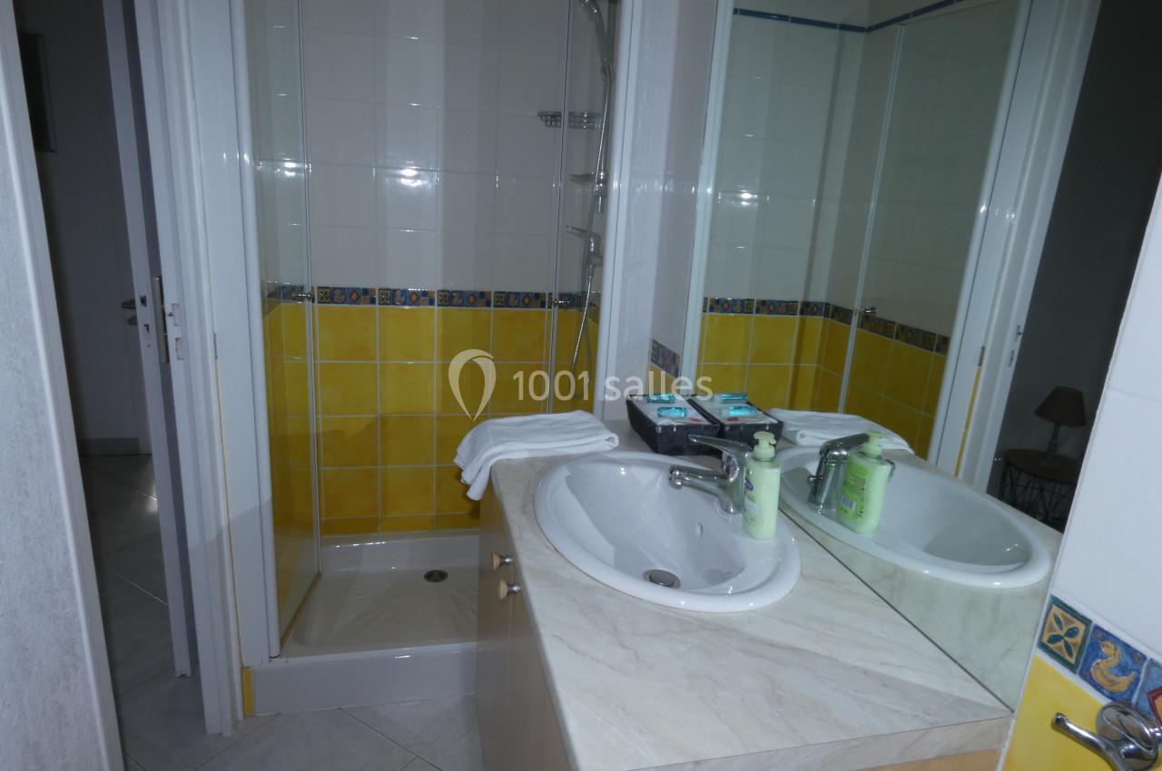 Salle de bain avec douche, double vasque sur plan en marbre, miroir et carrelage jaune et blanc.