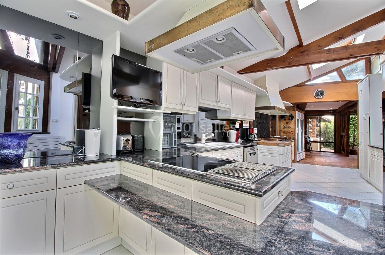 Cuisine moderne avec plan de travail en granit, électroménagers intégrés, poutres apparentes et grande luminosité naturelle.