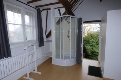 Salle de bain lumineuse avec baignoire encastrée sur estrade carrelée, poutres apparentes et grande fenêtre.