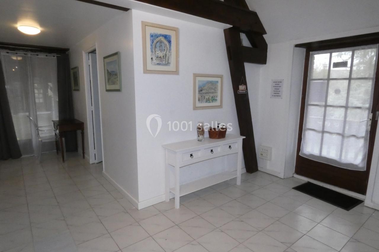 Entrée lumineuse avec sol en carrelage blanc, poutres apparentes, console blanche et porte-fenêtre vitrée.