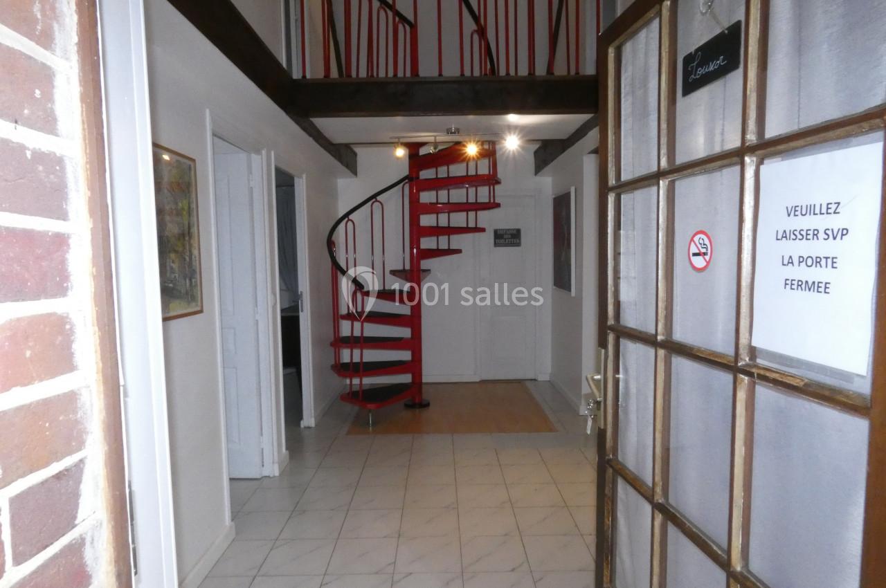 Entrée d'un bâtiment avec un escalier en colimaçon rouge, des murs blancs et une porte avec un panneau d'instructions.