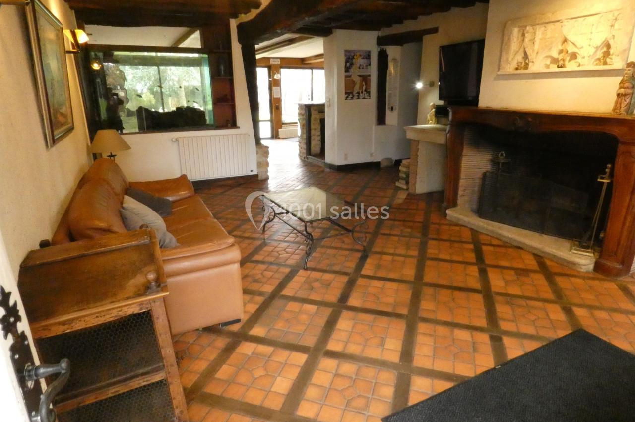 Salon rustique avec canapé en cuir, cheminée en pierre, poutres apparentes et sol en carreaux de terre cuite.