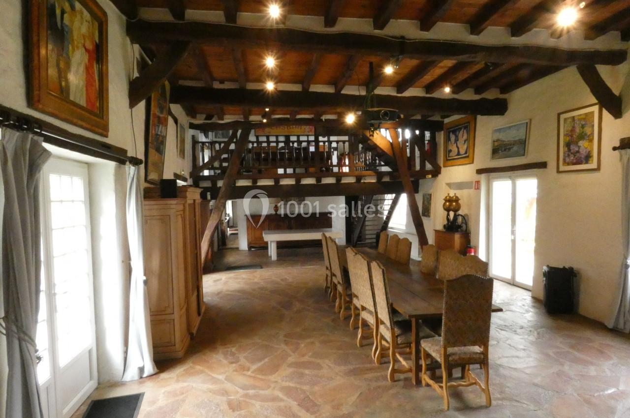 Salle à manger spacieuse avec une grande table en bois, poutres apparentes et mezzanine dans un style rustique.
