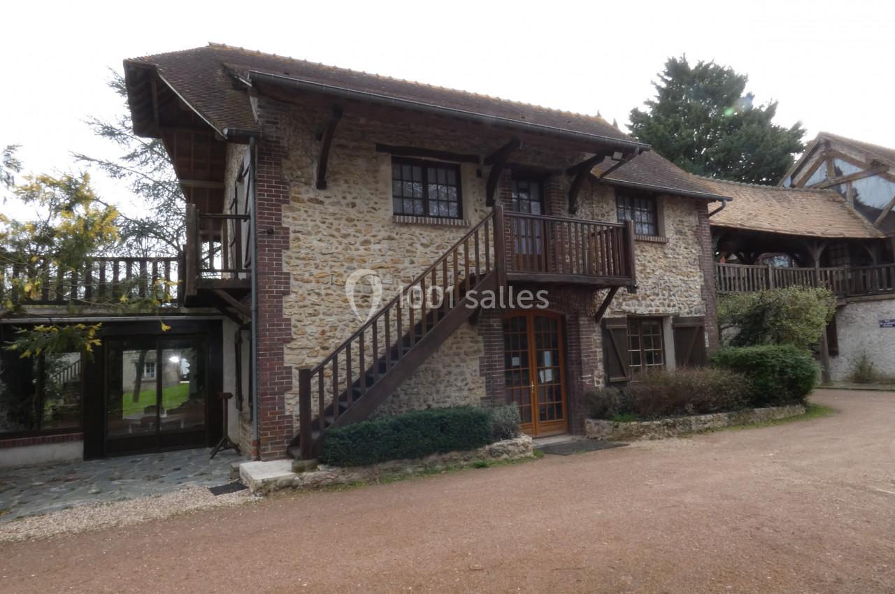 Maison en pierre avec balcon en bois, escalier extérieur et toit en pente, entourée de végétation.