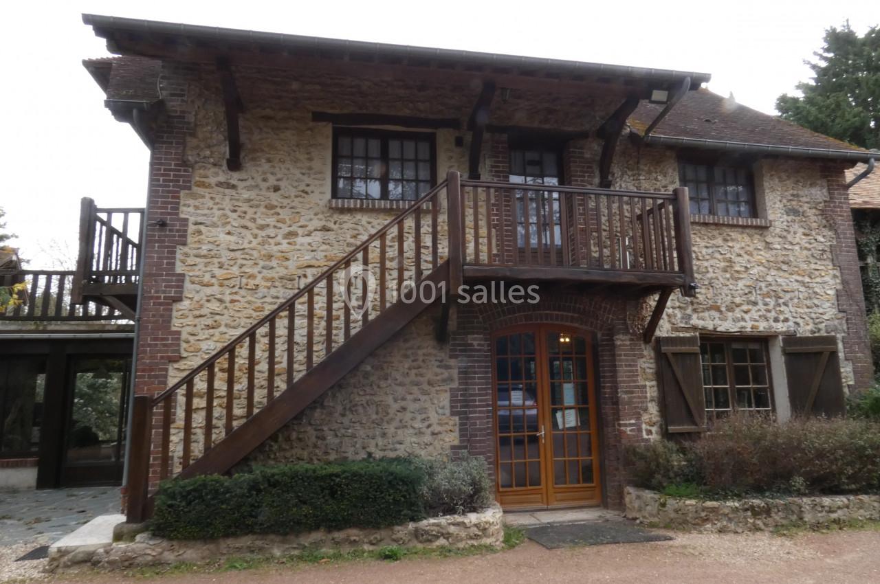 Façade d'une maison en pierre avec escalier extérieur en bois, balcon et volets en bois, entourée de végétation.