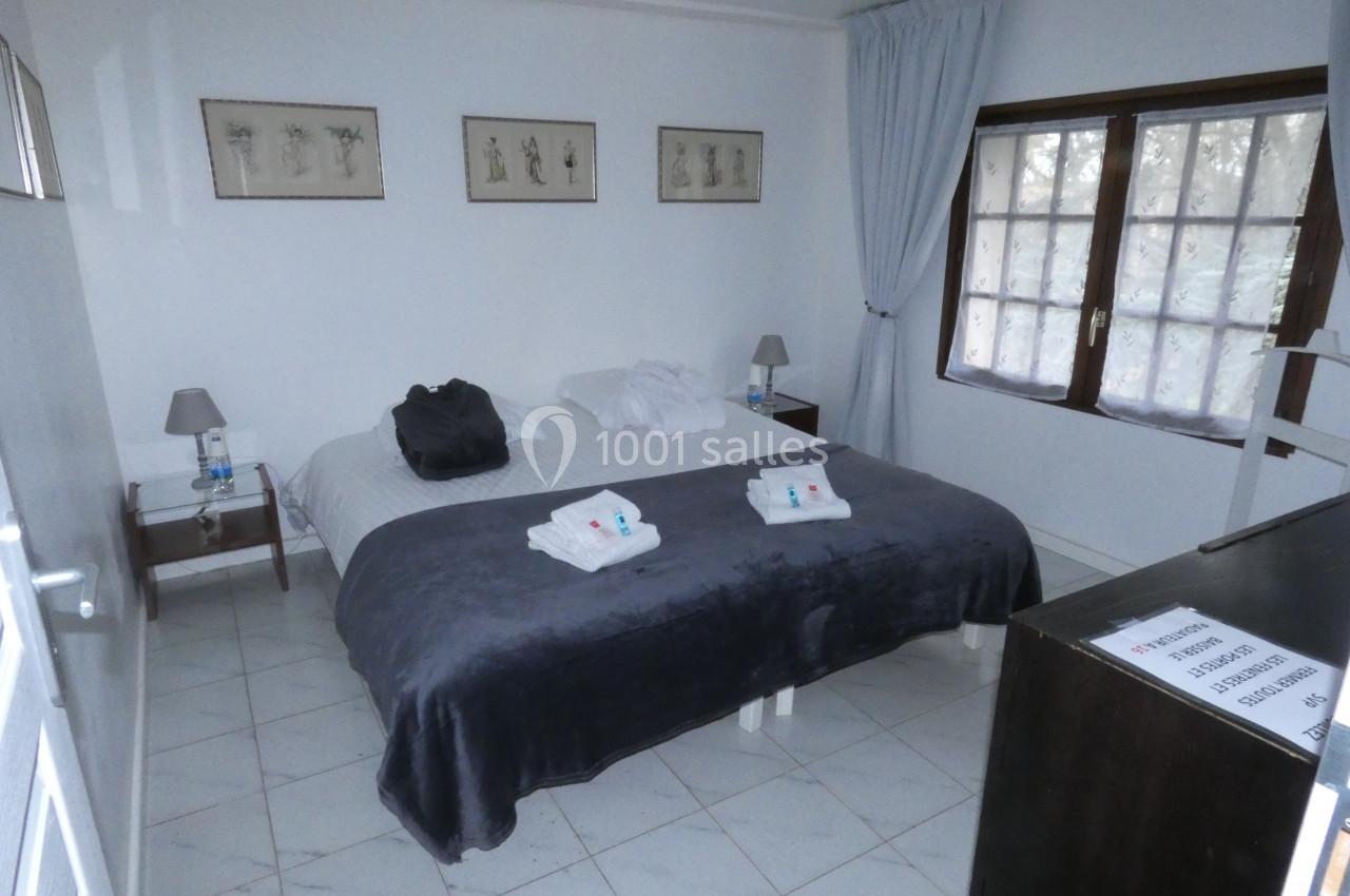 Chambre avec un lit double, draps gris, tables de chevet, lampes, fenêtres avec rideaux clairs et décorations murales.