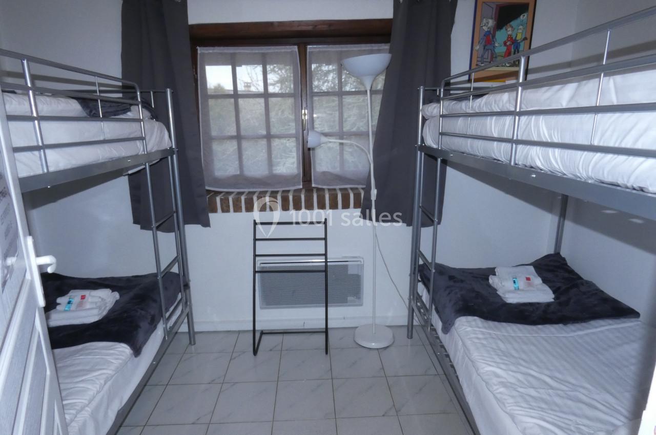 Chambre avec deux lits superposés, fenêtre centrale, rideaux gris, sol carrelé et lampadaire blanc.