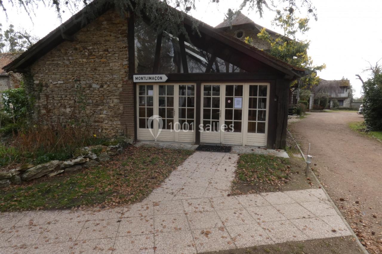 Bâtiment en pierre avec une façade vitrée, entouré de végétation, sur une allée pavée.