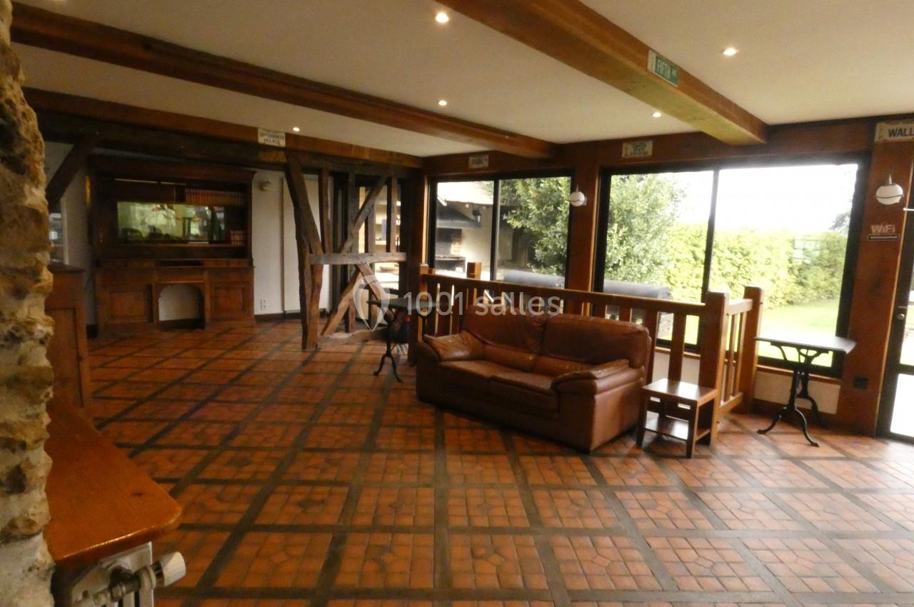 Salle lumineuse avec sol en carreaux, poutres apparentes, canapé en cuir et grandes baies vitrées donnant sur un jardin.