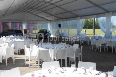 Terrasse extérieure avec tables et chaises en métal sur un sol en gazon synthétique, entourée de verdure.