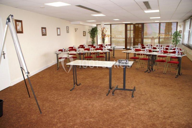 Salle de réunion équipée de tables, chaises, paperboard et projecteur, avec lumière naturelle et décoration sobre.