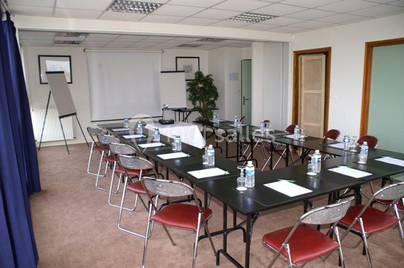 Salle de réunion équipée de tables, chaises, paperboards, bouteilles d'eau et matériel de présentation.