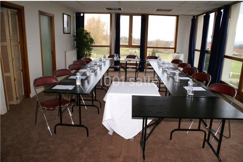 Salle de réunion lumineuse avec tables en U, chaises pliantes, bouteilles d'eau et vue sur un paysage extérieur.