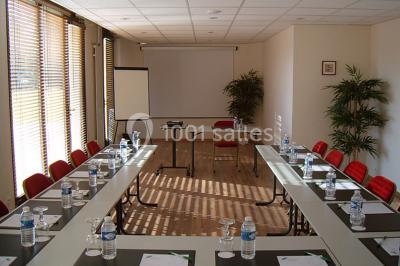 Terrasse extérieure avec tables et chaises en métal sur un sol en gazon synthétique, entourée de verdure.