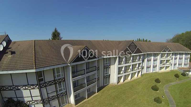 Bâtiment résidentiel à deux étages avec balcons, entouré d'une pelouse et d'arbres sous un ciel dégagé.