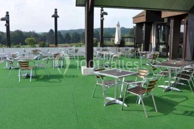 Terrasse extérieure avec tables et chaises en métal sur un sol en gazon synthétique, entourée de verdure.