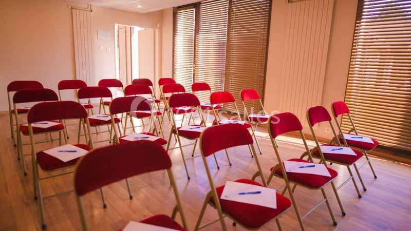 Salle lumineuse avec des chaises rouges alignées, chacune équipée d'un bloc-notes et d'un stylo.