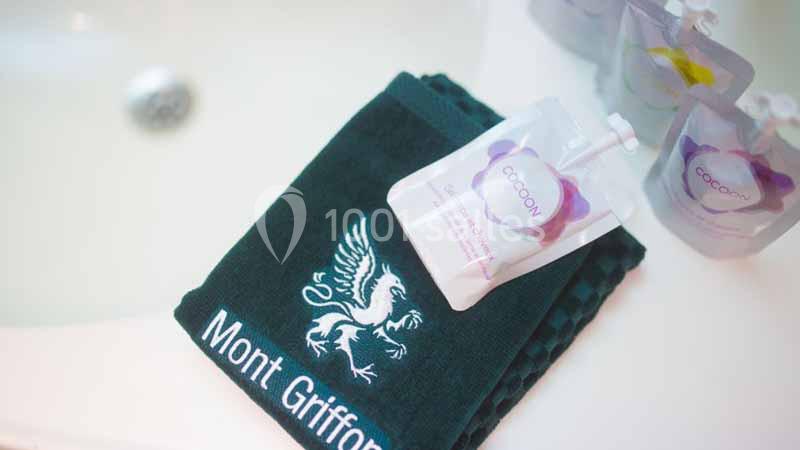 Serviette noire avec logo ’Mont Griffon’ posée près d'un lavabo, accompagnée de sachets de produits de soin.