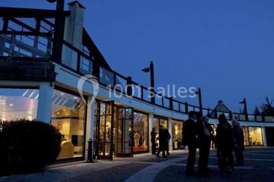 Terrasse extérieure avec tables et chaises en métal sur un sol en gazon synthétique, entourée de verdure.