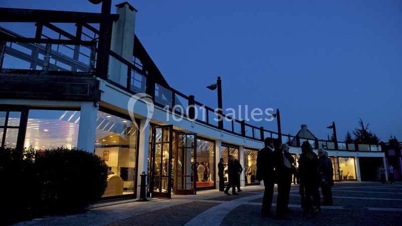 Façade d'un bâtiment moderne éclairé en soirée, avec des personnes discutant à l'extérieur.