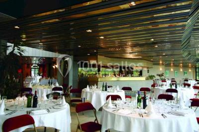 Terrasse extérieure avec tables et chaises en métal sur un sol en gazon synthétique, entourée de verdure.