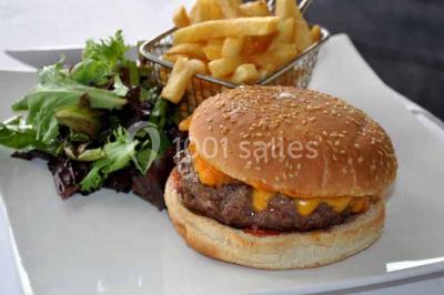 Terrasse extérieure avec tables et chaises en métal sur un sol en gazon synthétique, entourée de verdure.