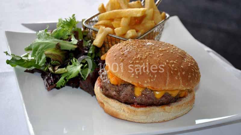 Burger au fromage servi avec des frites dorées dans un panier métallique et une salade verte sur une assiette blanche.