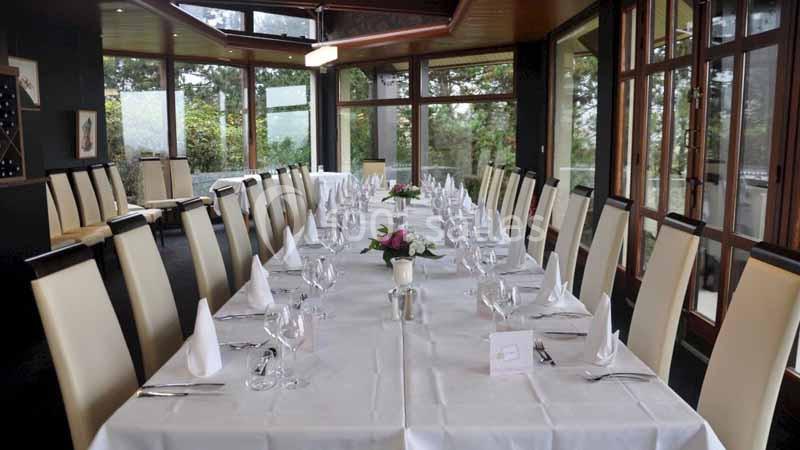 Salle de réception avec une longue table dressée, nappes blanches, serviettes pliées et décorations florales.