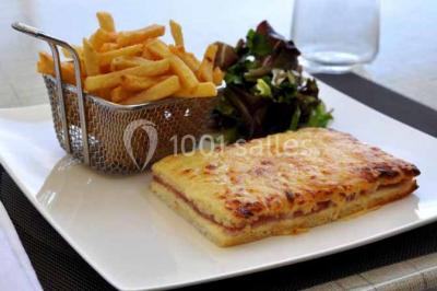 Terrasse extérieure avec tables et chaises en métal sur un sol en gazon synthétique, entourée de verdure.