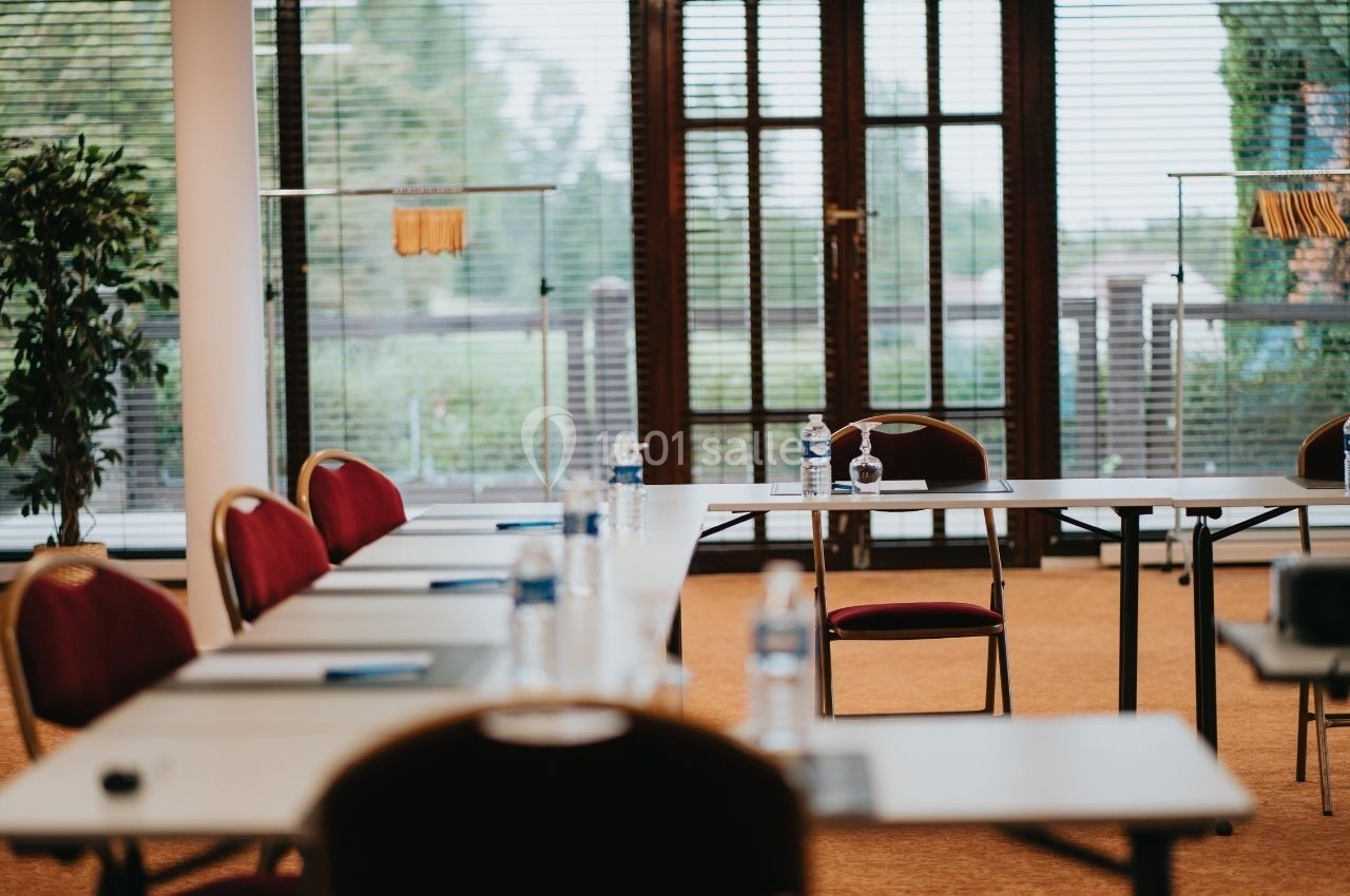 Salle de réunion lumineuse avec des tables blanches, des chaises rouges et des bouteilles d'eau sur les tables.
