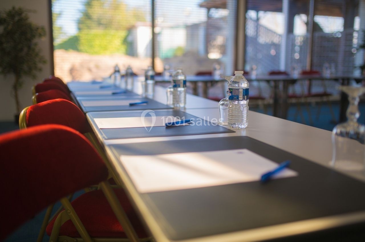 Salle de réunion avec des tables alignées, des chaises rouges, des bouteilles d'eau, des verres et des blocs-notes avec…