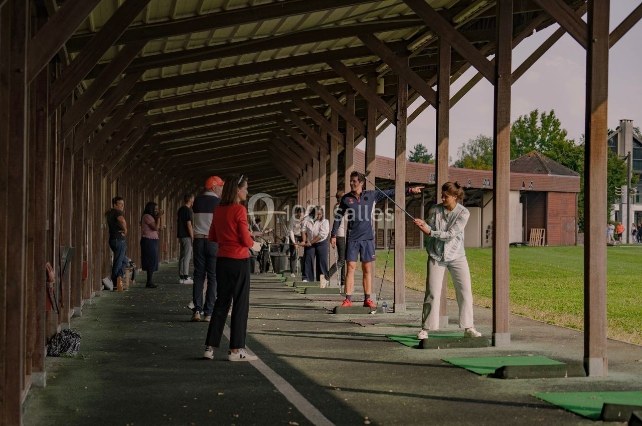 Des personnes s'entraînent au golf sous un abri, avec des instructeurs guidant les participants.