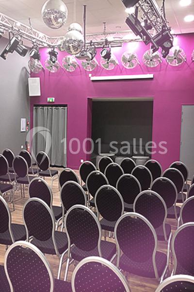 Salle de conférence avec chaises noires alignées, murs violets, projecteurs et boules disco suspendues au plafond.