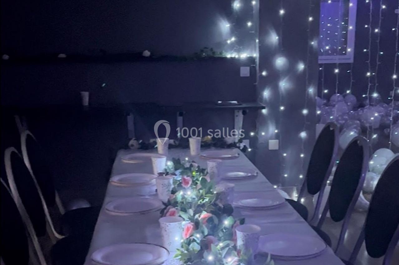 Table décorée avec une nappe blanche, guirlandes lumineuses, vaisselle et centre de table floral dans une salle sombre.